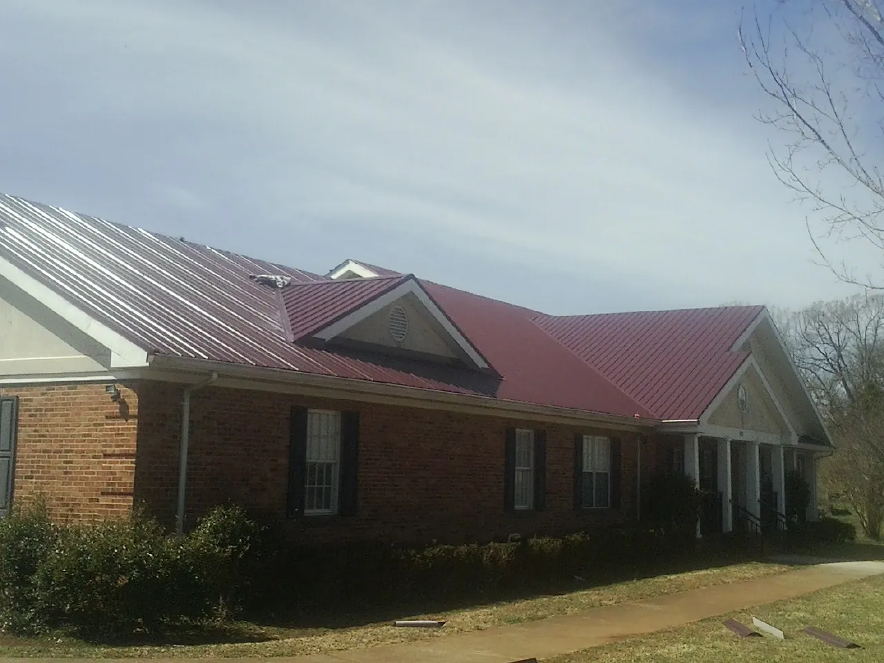 Red metal roof with gabled entries on a long brick building, from a Hail Damage Roof Repair job in Verdi